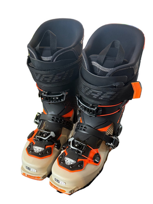 Pair of ski boots on a display stand with colorful ski equipment in the background.