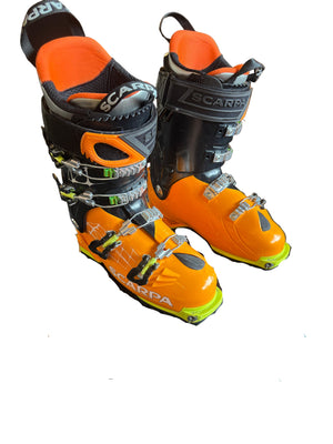 Orange and black ski boots on a wooden floor with a visible brand logo.