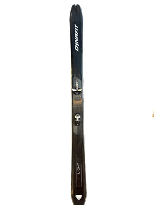 Two pairs of skis on a gray carpeted floor with a dog's paw visible.