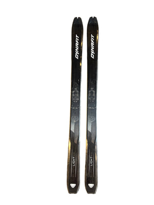 Two black skis with white branding on a gray textured surface.