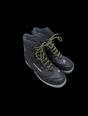 Black ski boots with green laces on a gray floor